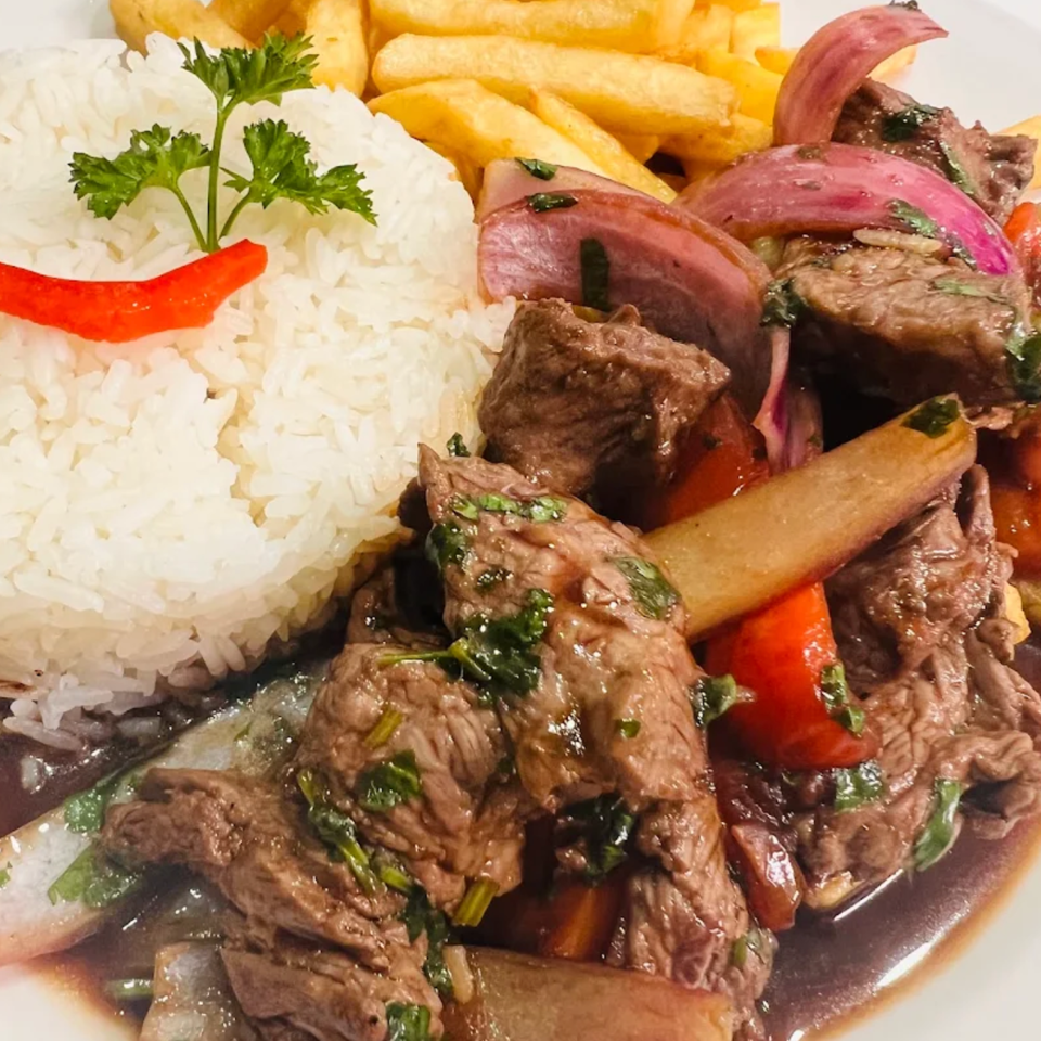 Plate of saucy beef strips with red onions and peppers, white rice, golden fries, parsley, and red pepper garnish.