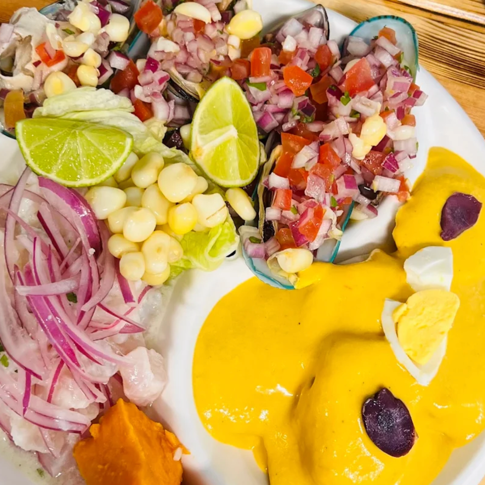 Peruvian seafood platter with mussels, ceviche, corn, red onions, lime wedges, sweet potato, and yellow chili sauce.