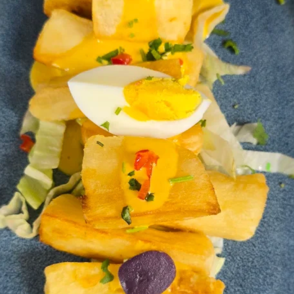 Layered golden pastry or pasta pieces with yellow sauce, lettuce, herbs, peppers, purple olives, and a sliced boiled egg on a blue plate.
