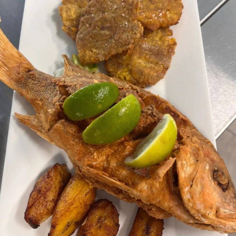 Crispy fried whole fish topped with lime wedges, served alongside golden fried plantains and fritters on a white plate.